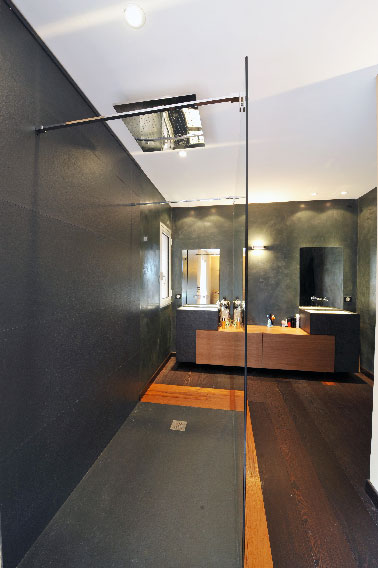Cette douche à l’italienne au design sobre avec ses murs gris anthracite faits à la chaux naturelle aspect marbré et son sol en parquet bambou offre une nouvelle perspective à la salle de bain.
