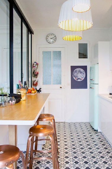 Les carreaux de ciment, chouchous de l'ambiance vintage dans la cuisine Les carreaux de ciment décorés au sol octroient à cette cuisine un aspect rétro indéniable relevé par plusieurs autres accessoires et meubles déco. Les tabourets usine couleur cuivre, le frigo Smeg bleu pastel, les suspensions « moules à gâteau » intérieur jaunit ou encore la cloison vitrée style atelier se marient à merveille avec le côté plus moderne du bar en bois clair.