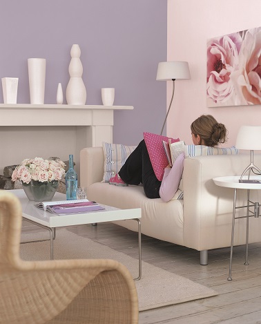 Dans ce salon, la peinture couleur parme se marie à merveille avec le canapé beige et la cheminée gris clair. Une ambiance sereine, douce et moderne, propice à la détente !