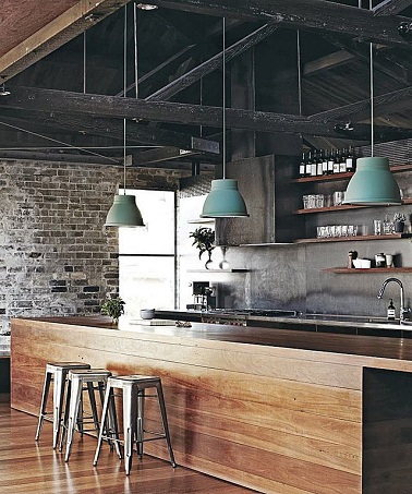 cuisine au design industriel mélange de bois et acier Le bois s'étend du parquet au plan de travail dans cette cuisine à la déco indus' discrète. Le mur en briques apparentes au fond de la pièce contraste avec la structure du plafond en acier noir. Les quelques accessoires se chargent d’accentuer le design usine. Les trois tabourets Tolix couleur métal amènent la touche de vintage tandis que la note de couleur est apportée par les suspensions bleu gris.