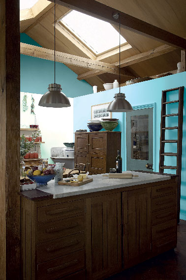 Miser sur une peinture de couleur flashy pour repeindre les murs d’une cuisine en bois, une bonne astuce pour moderniser la pièce. Dans cette cuisine c’est un bleu lumineux mis en contraste avec un pan de mur blanc qui réveille toute la cuisine.  Autre touche de modernité, la porte peinte dans un ton de vert/bleu très tendance. Peinture Astral teinte en machine à teinter.
