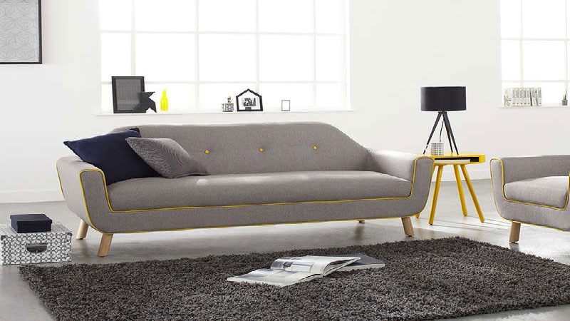 Un canapé en tissu gris perle aux lignes sobres bordé d'un liseré jaune tendre qui s'intègre parfaitement dans une décoration de salon design