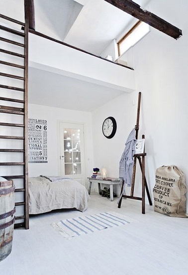  Dans une chambre avec mezzanine aménagée comme un atelier d’artiste, la peinture blanche s’égaye de teintes naturelles avec le linge de lit en lin et le bois omniprésent avec l’échelle et les poutres.
