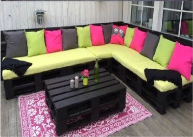 Salon de jardin en palettes peintes en noir et coussins vert et rose Un salon de jardin en palette bois comprenant une grande banquette en L et une table basse fabriquée simplement avec deux palettes superposées. Le tout est peint en noir mat et décoré de coussins vert pomme qui recouvrent la banquette.