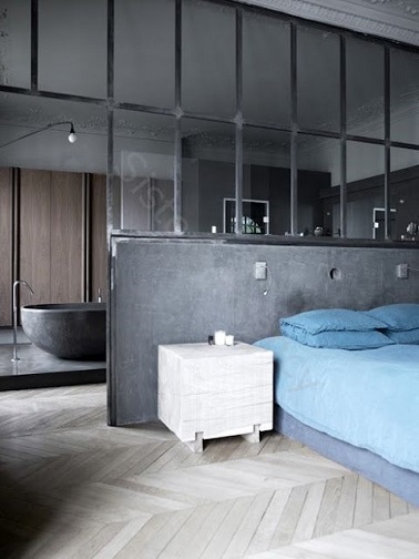 Dans cette suite parentale au style industriel, l’ambiance est à la relaxation. Le petit mur gris qui sert à la fois de tête de lit et de séparation avec le point d’eau de la pièce vient contraster avec le parquet clair en bois. La baignoire design gris anthracite qui apparaît dans la continuité du lit permet de renforcer l’esprit zen et détente de la pièce. Une chambre qui a de la suite dans les idées ! 