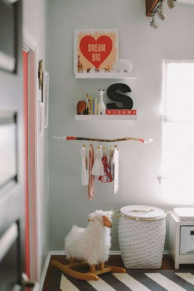Une idée déco chambre tendance et originale pour bébé Orange et gris, le duo gagnant de cette chambre de petite fille. Dans ce petit coin rangement, deux petites étagères blanches permettent de soutenir les petits livres pour la lecture du coucher mais aussi des objets déco. L’initiale ainsi que le prénom du bébé constituent des éléments décoratifs personnalisant la pièce tout comme le tableau rappelant la couleur orangée de certains éléments. Dans un domaine pratique et esthétique, une branche bois constitue la suspension idéale pour pendre les cintres et les vêtements de bébés. Une astuce fonctionnelle pas chère et facile à faire !