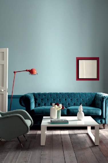  Ce salon adopte une peinture bleu sur ses murs. Pour peindre le haut du mur une teinte de bleu gris pour sa douceur contraste avec le bleu du soubassement coordonné au canapé de style. Avec du rouge et blanc pour les accessoires, un petit salon tendance rétro chic. Peinture Little Greene.