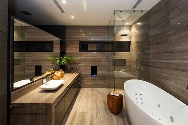 Elégante salle de bain revêtue de bois sur tous ses murs, le sol et le plan vasques qui donne une place de choix à la grande baignoire balnéo et à sa douche italienne fermée de 3 parois de verre.