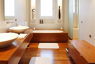 Aménagement luxueux dans une salle de bain avec du chêne doré pour le sol le plan vasque et l’habillage de la baignoire mettant une focal sur les 2 grandes vasques blanches.