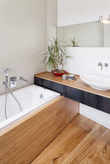 Une petite salle de bain à l’aménagement optimisé avec un plan vasque en bois encastré sur le bout de la baignoire au tablier recouvert du même bois à l’unisson avec le sol
