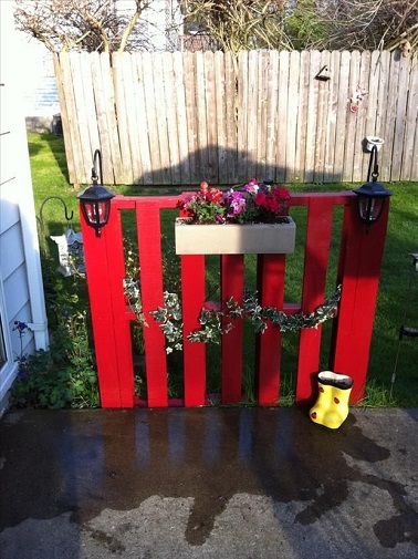 Une clôture en palette pour donner du cachet à la terrasse Purement décorative, cette petite barrière palette vient illuminer tout l’extérieur. Peinte dans un rouge vif, elle apporte une touche de modernité à la terrasse. Simplement posée sur le sol elle arbore une jolie jardinière délicate ainsi que deux lumières d’extérieur qui viennent lui apporter du charme et une utilité qui sort du simple esthétisme. Comme quoi un seul petit coup de peinture suffit à relooker vos vieilles palettes en vrai objet déco mignon et pas cher. Source : dumpaday.com