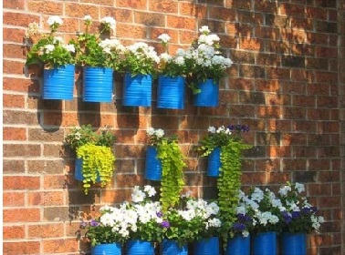 Pots fleurs bleus en boites de conserve sur un mur du jardin en brique rouge Les boites de conserve s'offrent une 2ème vie recyclées en pots de fleurs dans le jardin ou le balcon. Un coup de peinture bleue sur les boites et les fleurs sont des les pots.