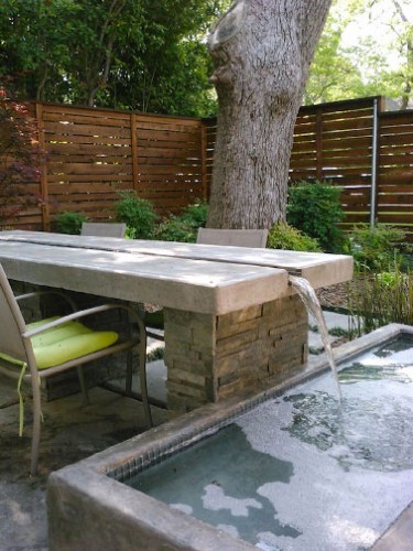 Déco de rêve sur une terrasse zen avec une table de jardin traversée par un circuit d’eau s’écoulant dans le bassin proche pour mieux y revenir grâce à une installation d’eau en circuit fermé.