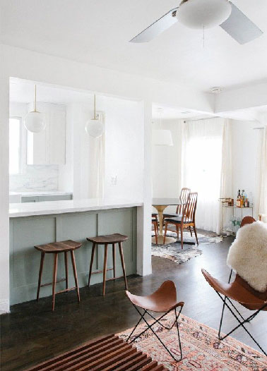 Adoptant les couleurs pastel et le bois une cuisine ouverte implantée en U avec un bar pour séparer du salon