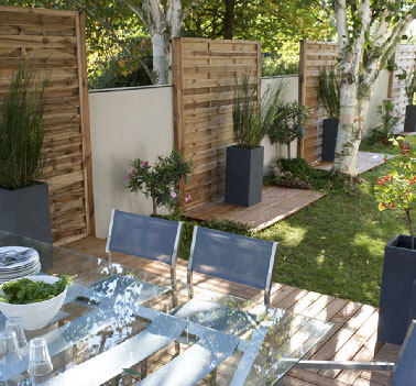 Traitées contre l'humidité, les dalles de cette terrasse en bois  prolonge son caché naturel par des panneaux de lames en pin fixés sur le mur du jardin 