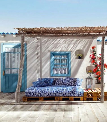 L’art d’utiliser des palettes bois pour meubler sa terrasse avec une banquette prolongée d’une table basse. Des coussins bleu et blanc, des canisses pour s’abriter du soleil, une déco de terrasse que l’on aimerait faire sienne.