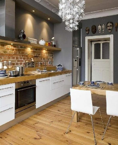 Pour la déco de cette grande cuisine aux allures de maison de campagne se conjuguent le chic d’une cuisine blanche, la neutralité du gris avec la peinture sur chacun des murs et l’impression de confort avec le bois du plan de travail et du sol.