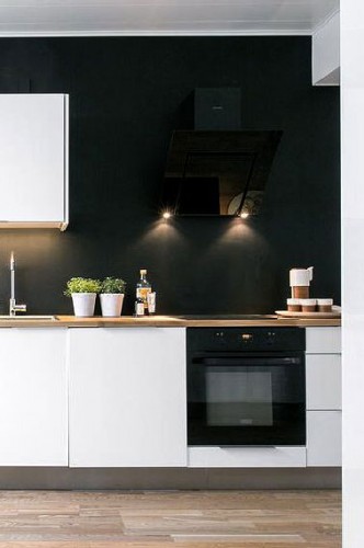 Une déco haute couture en blanc et noir pour une cuisine moderne. Sur le mur de la crédence une peinture noir satin sublime la zone cuisson de cette cuisine blanche sans nuire à sa luminosité. Agrémentée de  2 ou 3 spots le mur noir révèle son élégance. 