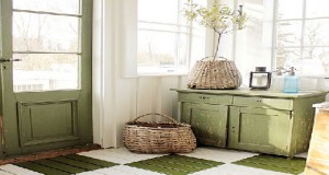 Décoration accueillante pour l’entrée d’une maison de campagne aménagée avec un meuble de rangement et un sol en bois repeints en vert et lin.
