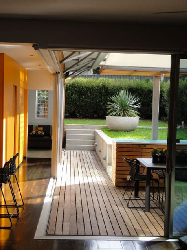 Un accès direct à la cuisine d'été par une jolie petite terrasse en bois mise en valeur par le carrelage et les murets de briques. Un aménagement et un choix de revêtement de sol qui optimise l’espace restreint depuis la maison.