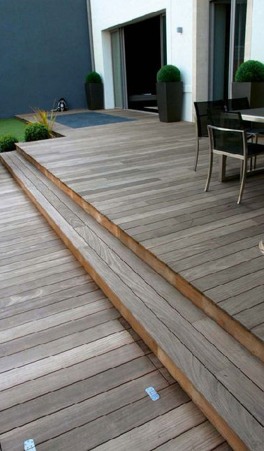 Assurant le confort extérieur d'une maison moderne, une terrasse en ipé aménagée sur deux niveaux donnant un accès direct à la pelouse. encastré dans le bois, un carré de galets pour l’effet zen 