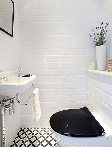 Dans des WC dépourvus de fenêtre, un carrelage métro blanc posé sur toute la hauteur des murs égayé par les motifs noirs du carrelage au sol qui trouvent un écho avec l'abattant WC de la cuvette suspendue
