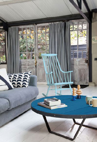 Une peinture en 2 teintes de bleu pour repeindre un fauteuil et une table basse dans un salon  aux murs et rideaux gris crée un contraste dynamique à peu de frais. Peinture couleur bleu récif pour le fauteuil en bois, couleur Lumière d'Azur satin sur le plateau de table basse en bois et noir satin pour les pieds en fer. Peinture Rénovation Design & Vous Tollens chez Castorama.