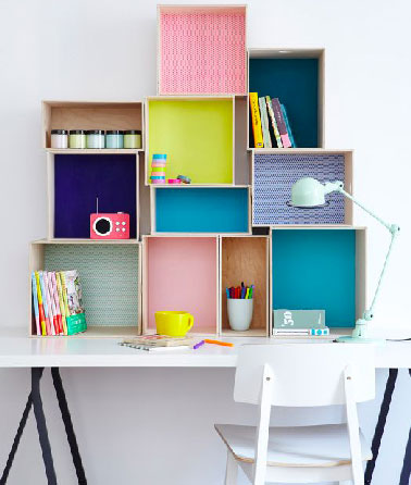 Pour ce bureau, une pile de boîtes de rangement mises en couleur pour que l'enfant range crayons posées en mural au dessus du plateau. une idée pratique et déco pour gagner de la place dans la chambre. 