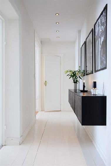 Design en noir et blanc pour la déco d’un couloir en prise directe avec l’entrée de l’appart. En contraste avec les murs et le parquet peints en blanc, un meuble suspendu laqué noir sert au rangement des clés et sacs. 