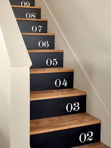 Un relooking d'escalier en bois fait sur le mode ludique avec les marches revernies et contremarches peintes en noir avec pochoir chiffre blanc.