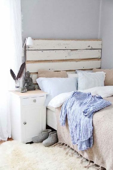 En parfaite harmonie avec les couleurs pastel de la chambre, la tête de lit palette est ici dépouillée de ses traverses en bois, puis recouverte d’une peinture blanche poncée sur les bords pour donner un aspect vieilli au bois.