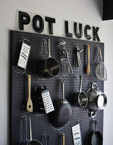 Crochés sur une plaque d'isorel recouverte d'une peinture noire casseroles et ustensiles se rangent de manière pratique dans une cuisine où les meubles de rangement font défaut.