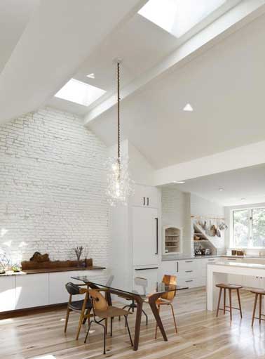 Pour mettre en valeur l’architecture de la pièce, cette cuisine ouverte sur la salle à manger  opte pour une peinture blanche de la même teinte que les meubles. Le parquet, les chaises en bois assurent l’ambiance chaleureuse de la pièce. 