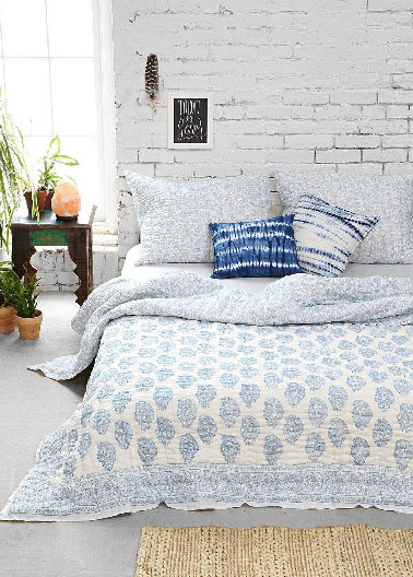 Une décoration de chambre adulte qui mixte matériaux bruts et couleurs claires pour créer une ambiance paisible et lumineuse. Les murs de briques sont recouverts d’une peinture blanche tandis que sol gris perle sublime le bleu et blanc du linge de lit. 