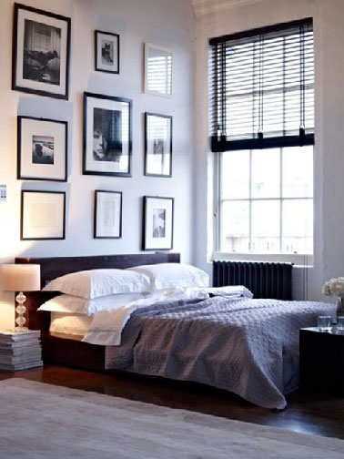 Une chambre parentale blanche et noir qui orchestre sa décoration en fixant un point fort sur l’espace du lit. Contrastant avec les murs blancs,  le noir s’impose pour la tête de lit surmontée du composition de cadres photos eux aussi noirs.