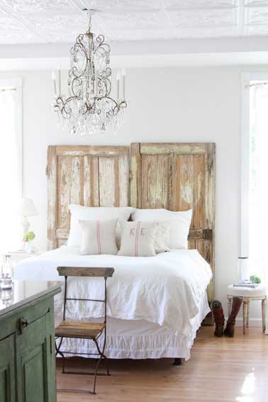 La simplicité se fait chic dans une chambre blanche avec une tête de lit aménagée avec 2 portes aspect bois flotté posées à la tête du lit sans autres transformations. Point d’orgue pour un style bohème chic, le lustre à facettes en verre blanc.