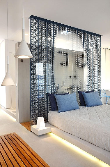 Une suite parentale de 45 m2  à vous faire rêver d’évasion à Athènes. Aménagée par l'agence A31 architecte, cette chambre luxueuse dissimule derrière la cloison de verre installée à la tête du lit, une douche italienne aux murs enduits de ciment clair sublimant le sol et receveur en teck. 