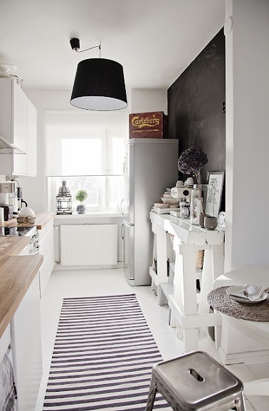 Dans cette cuisine toute en longueur, mettre un tapis aux rayures horizontales au sol donne l'illusion d'un espace plus large. En noir et blanc ça rompt l'effet couloir.