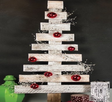 Ce sapin de Noël en bois de palette recyclée a été repeint en blanc pour donner un effet neige de saison. Les grosses boules rouges en déco créent un contraste qui rappelle le code couleur du sapin de Noël traditionnel.