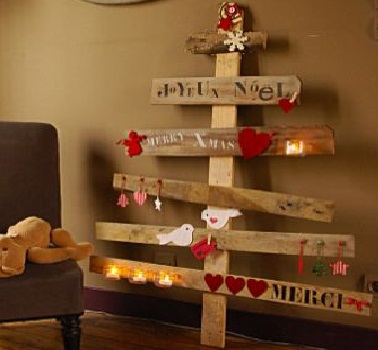 Comme un arbre de Noël en palettes recyclées, ce sapin en bois de cagette adopte un look simple et minimaliste. Les décorations sont collées et clouées sur les planches et des phrases sont peintes à même le bois.