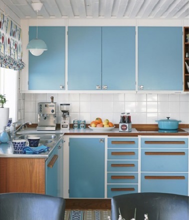 Des portes de cuisine bleu pour un décor vintage Lorsque qu’une cuisine bleu adopte un look vintage, on craque ! Associant joliment portes de meubles bleu azur équipées de poignées en bois, carrelage blanc et store bateau imprimé rétro, cette cuisine convainc par son élégance
