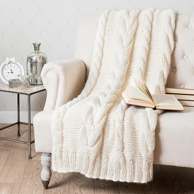 Un plaid tricoté en grosses mailles couleur blanc cassé.