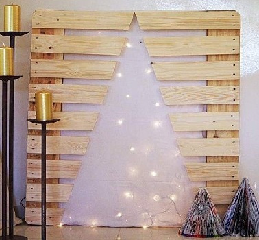 Un sapin de Noël découpé dans une palette en bois et décoré avec une guirlande lumineuse blanche pour une décoration très épurée.