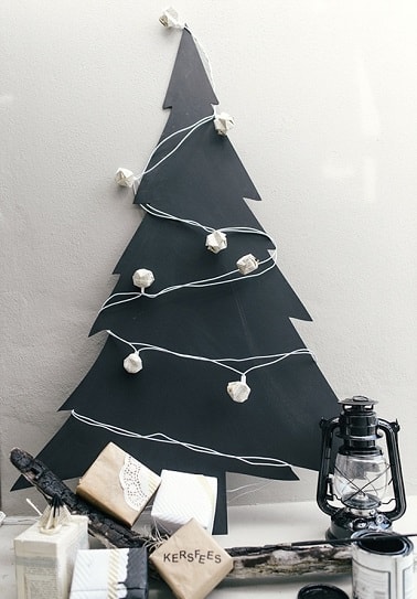 La forme de ce sapin de Noël est découpée dans une planche de bois peinte en noire pour un sapin contemporain original à souhait avec des guirlandes blanches design.