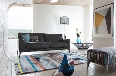 Dans ce salon au mobilier au look design, le canapé en cuir noir s'accorde avec le tapis en laine ethnique, la table basse design et le repose pieds recouvert d'un tissu imprimé reprenant les couleurs du tapis