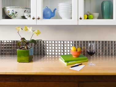Posé sur le bord du plan de travail, une crédence en carrelage adhésif aspect inox brillant de 25cm de haut