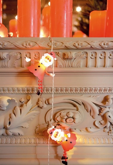 Cette guirlandes met en lumière des petits pères Noël qui semblent comme escalader la commode du salon. Une décoration de Noël enfantine et très mignonne pour la maison.