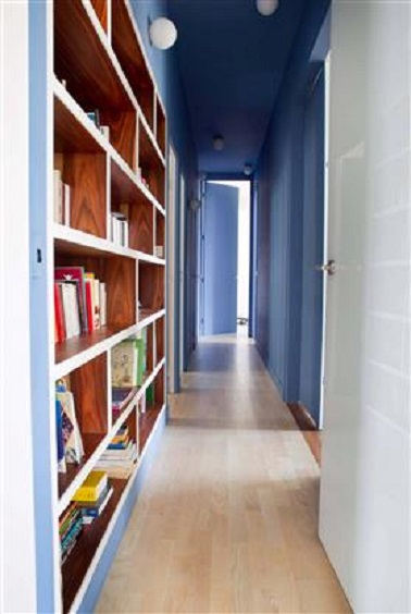Dans ce long couloir, une bibliothèque en bois vient s'insérer sur l'un des murs peints en bleu. Une idée déco couloir fonctionnelle et esthétique comme jamais.
