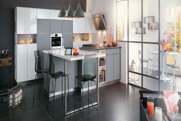 Cette petite cuisine américaine sépare l'espace grâce à un plan de travail gris en L et une extension mange debout blanc.