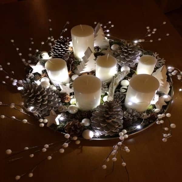 Un plateau lumineux composé de bougies, de pommes de pin, de branches et de petits objets déco pour décorer la table de Noël.